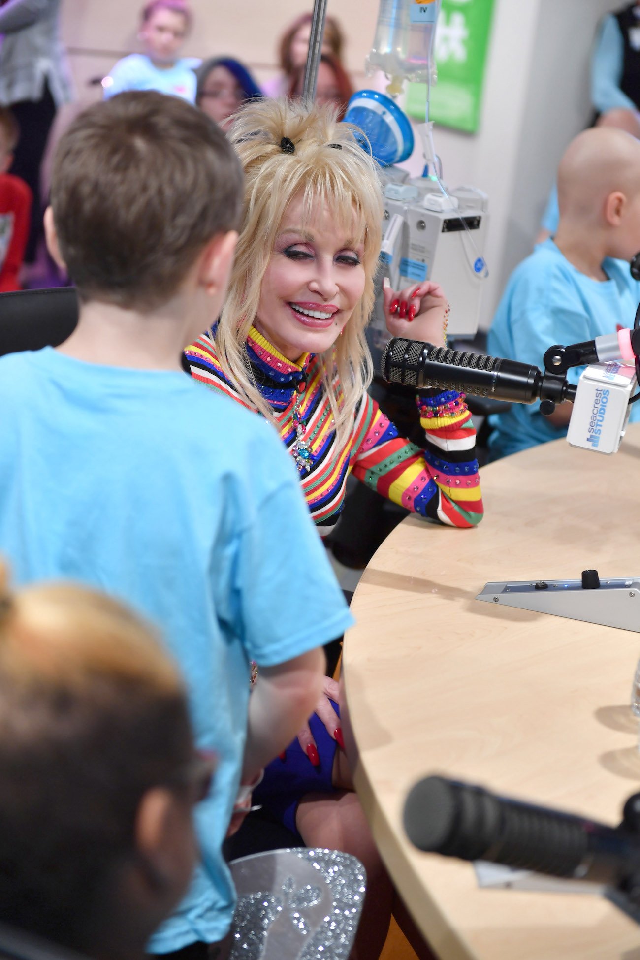 Dolly Parton smiles as she speaks into a microphone and looks at a boy standing next to her