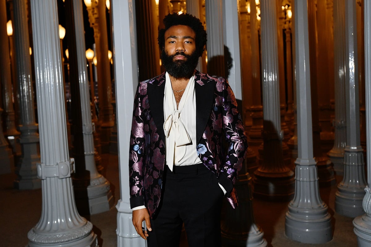 Donald Glover posing in a purple suit with a hand in his pocket.