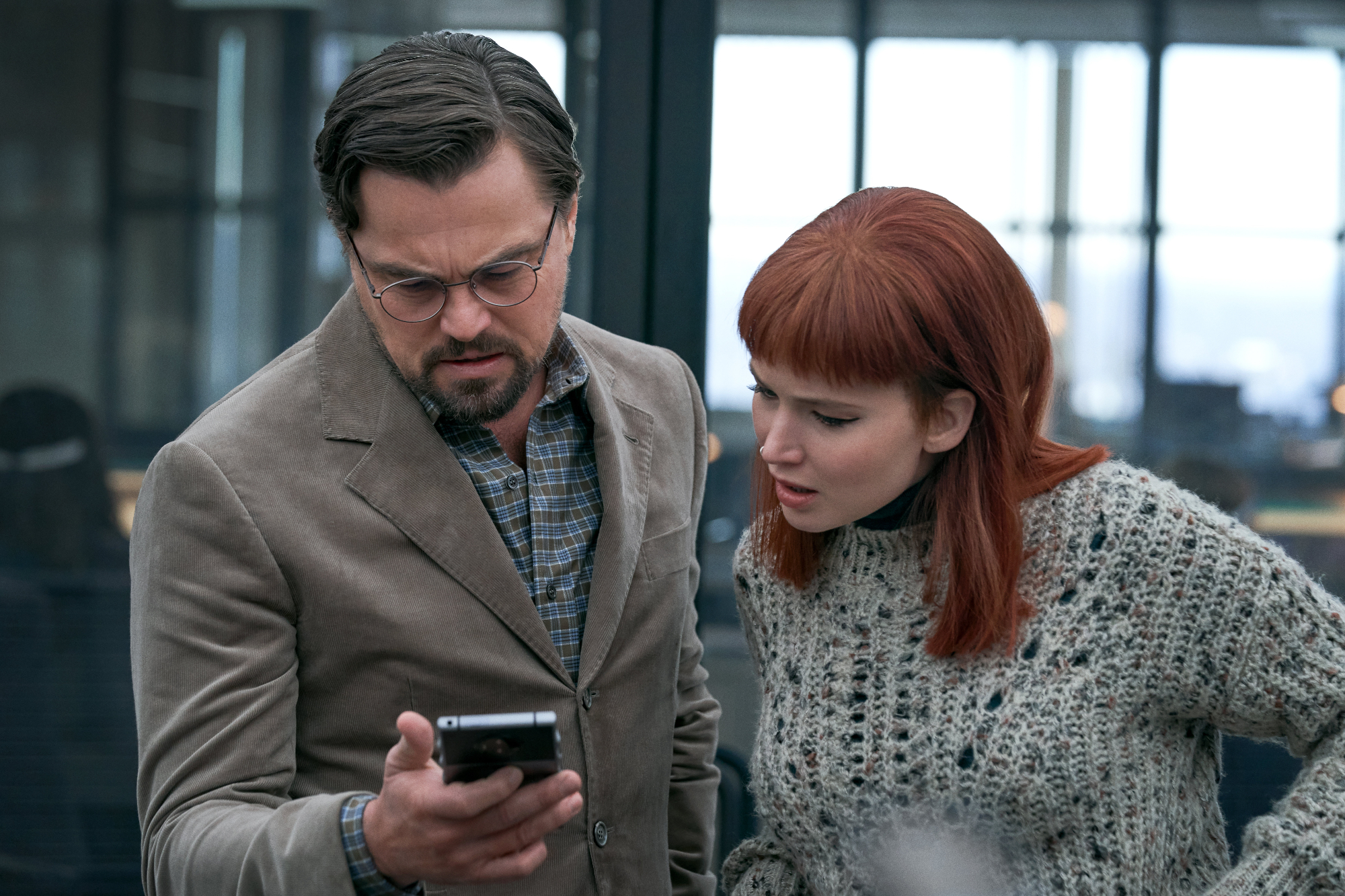 'Don't Look Up' stars Leonardo DiCaprio as Dr. Randall Mindy and Jennifer Lawrence as Kate Dibiasky looking at a cell phone