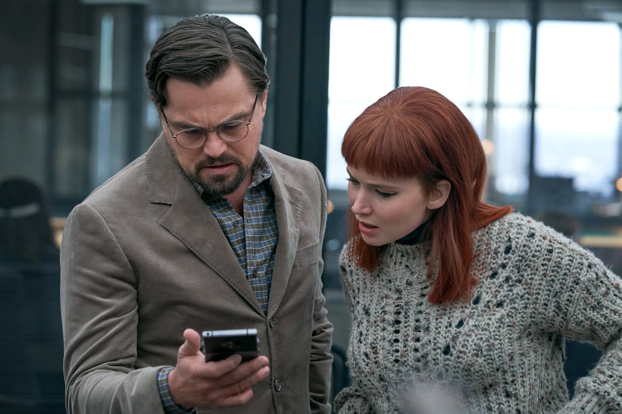 Leonardo DiCaprio as Dr. Randall Mindy and Jennifer Lawrence as Kate Dibiasky in Don't Look Up looking at a cellphone