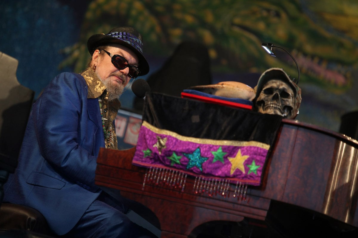 Dr. John performs on stage playing the piano with a skull on top of it.