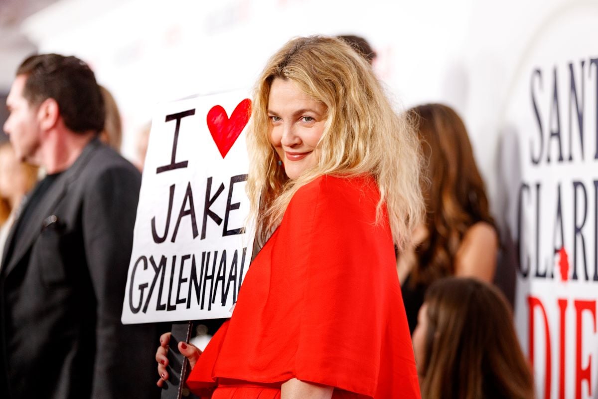 Drew Barrymore, in red, holds a sign that says "I love Jake Gyllenhaal"