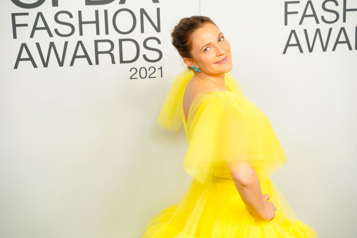 Drew Barrymore looks over her shoulder, wearing a bright yellow dress