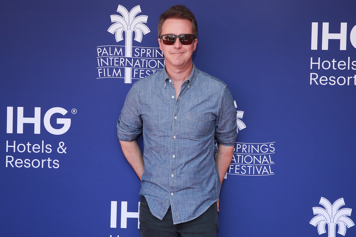 Edward Norton wearing a button up shirt and sunglasses while smirking