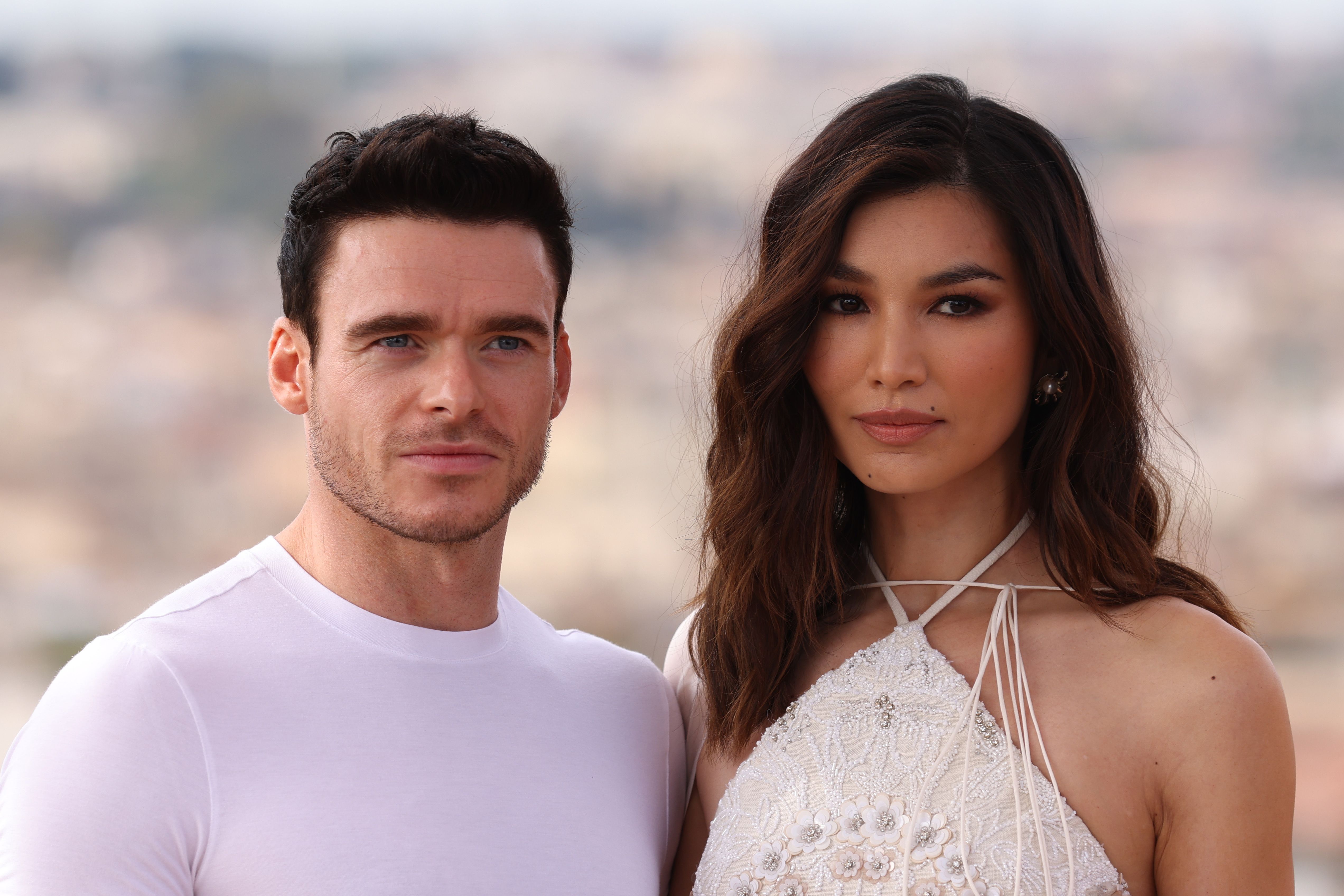 Marvel's 'Eternals' stars Richard Madden and Gemma Chan pose for a photo. Madden wears a white shirt. Chan wears a white dress with patterned flowers on it.