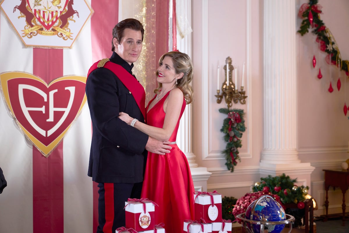 Jen Lilley in red dress poses with Brendan Fehr, in uniform, in 'Royally Wrapped for Christmas'
