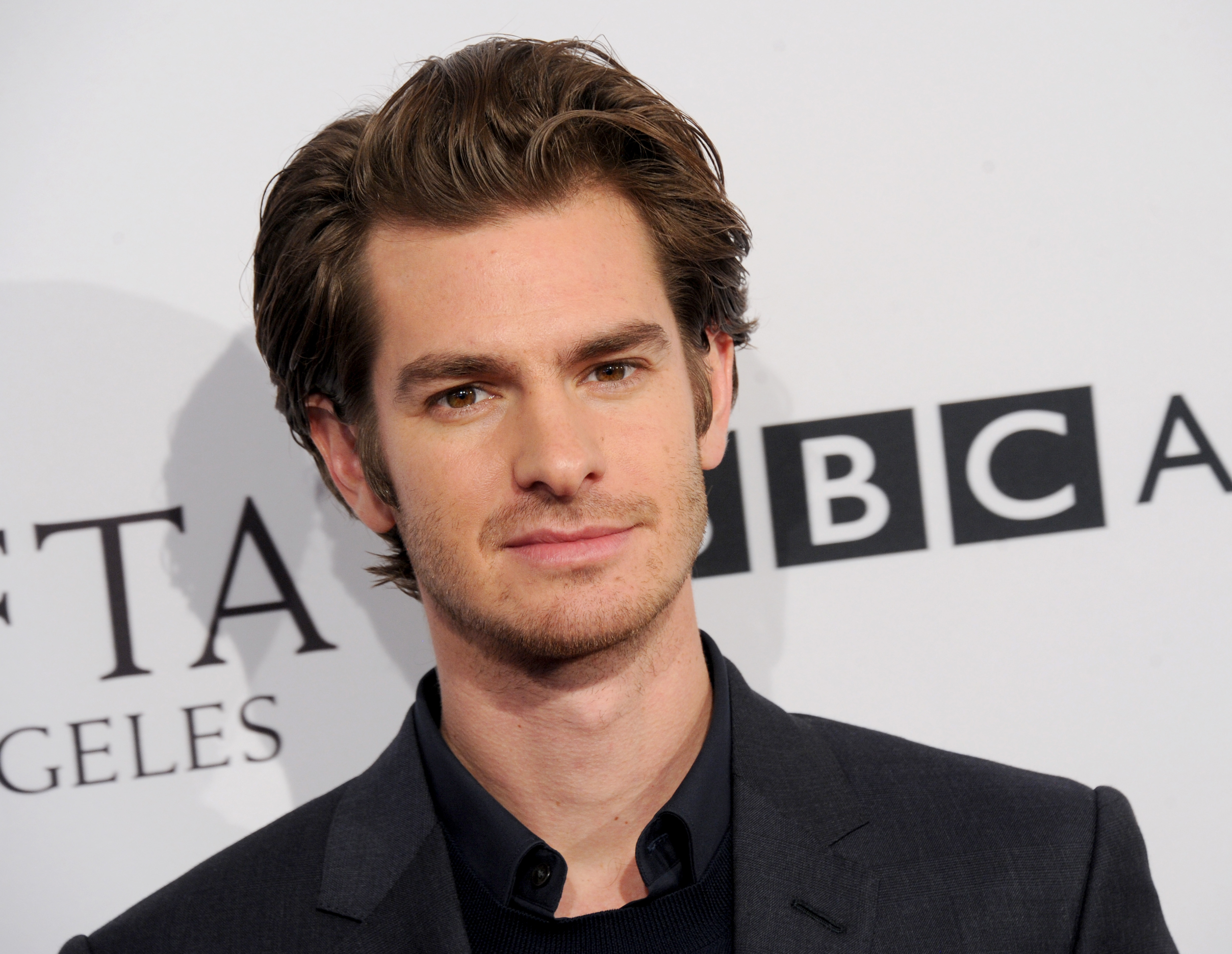 Andrew Garfield, who may be in 'Spider-Man: No Way Home' along with Tobey Maguire, wears a dark gray suit over a black button-up shirt.