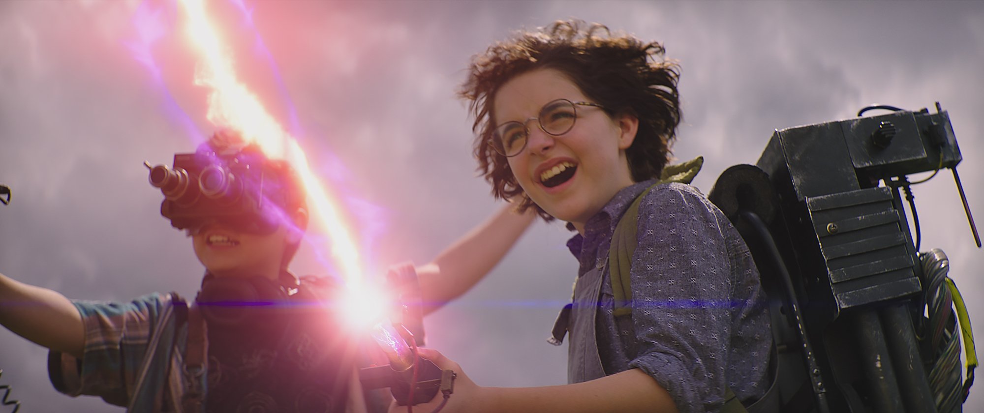 'Ghostbusters: Afterlife' with Phoebe (Mckenna Grace) and Podcast (Logan Kim) firing a proton pack with goggles