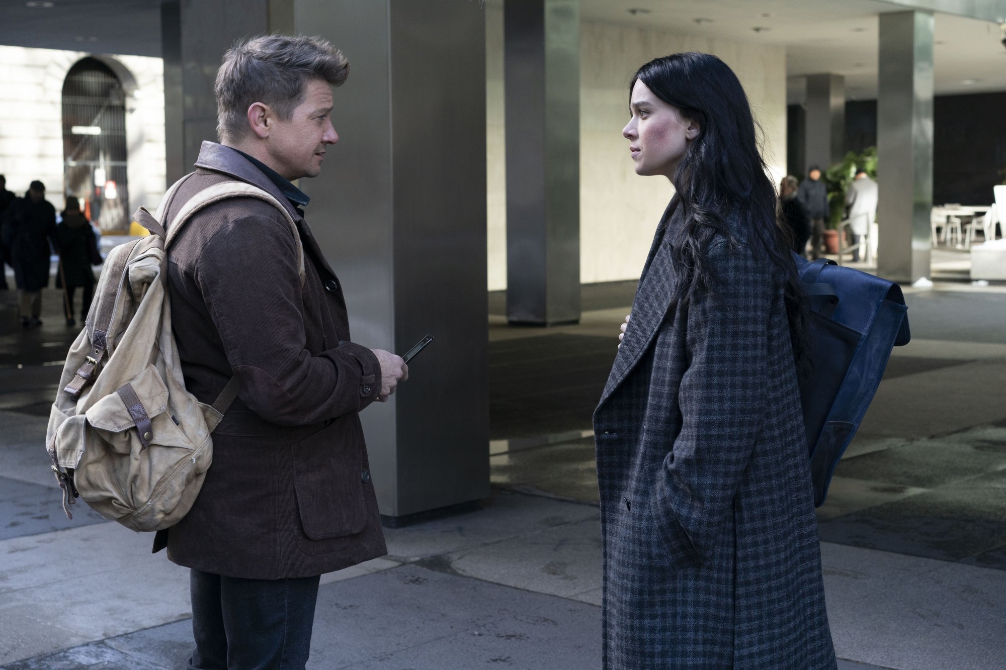 Jeremy Renner and Hailee Steinfeld as Clint Barton and Kate Bishop in Marvel's 'Hawkeye' show on Disney+. They're facing one another on a sidewalk in New York City.
