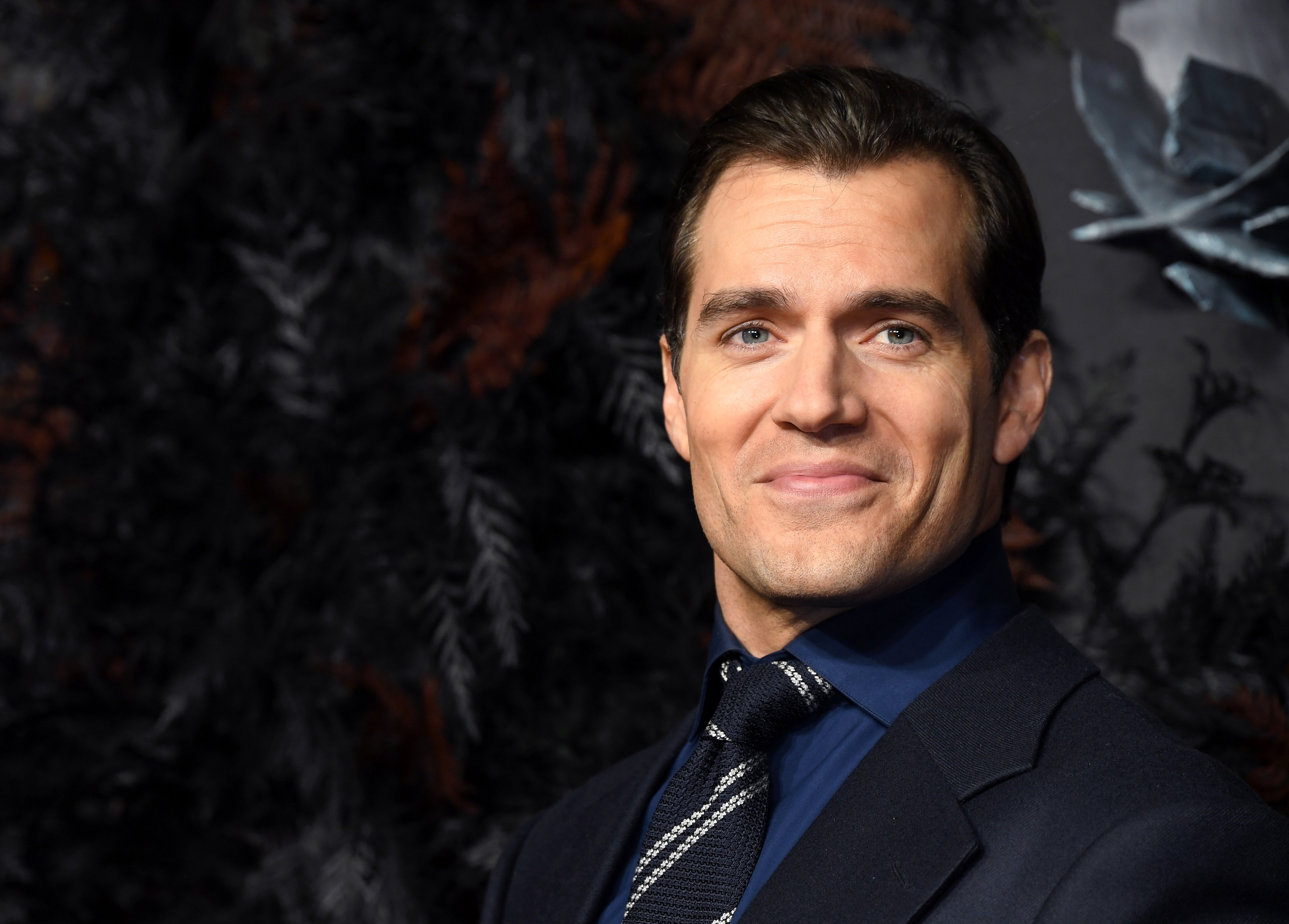 'Superman' actor Henry Cavill wears a black suit over a blue shirt and white striped blue tie.