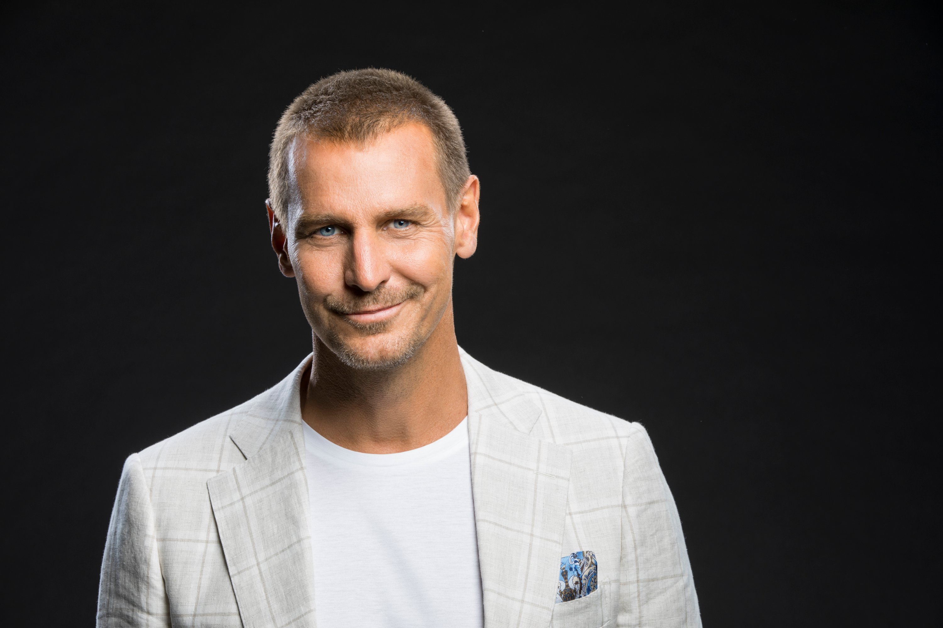 'The Bold and the Beautiful' actor Ingo Rademacher wearing a grey jacket and white shirt, and standing in front of a black backdrop.