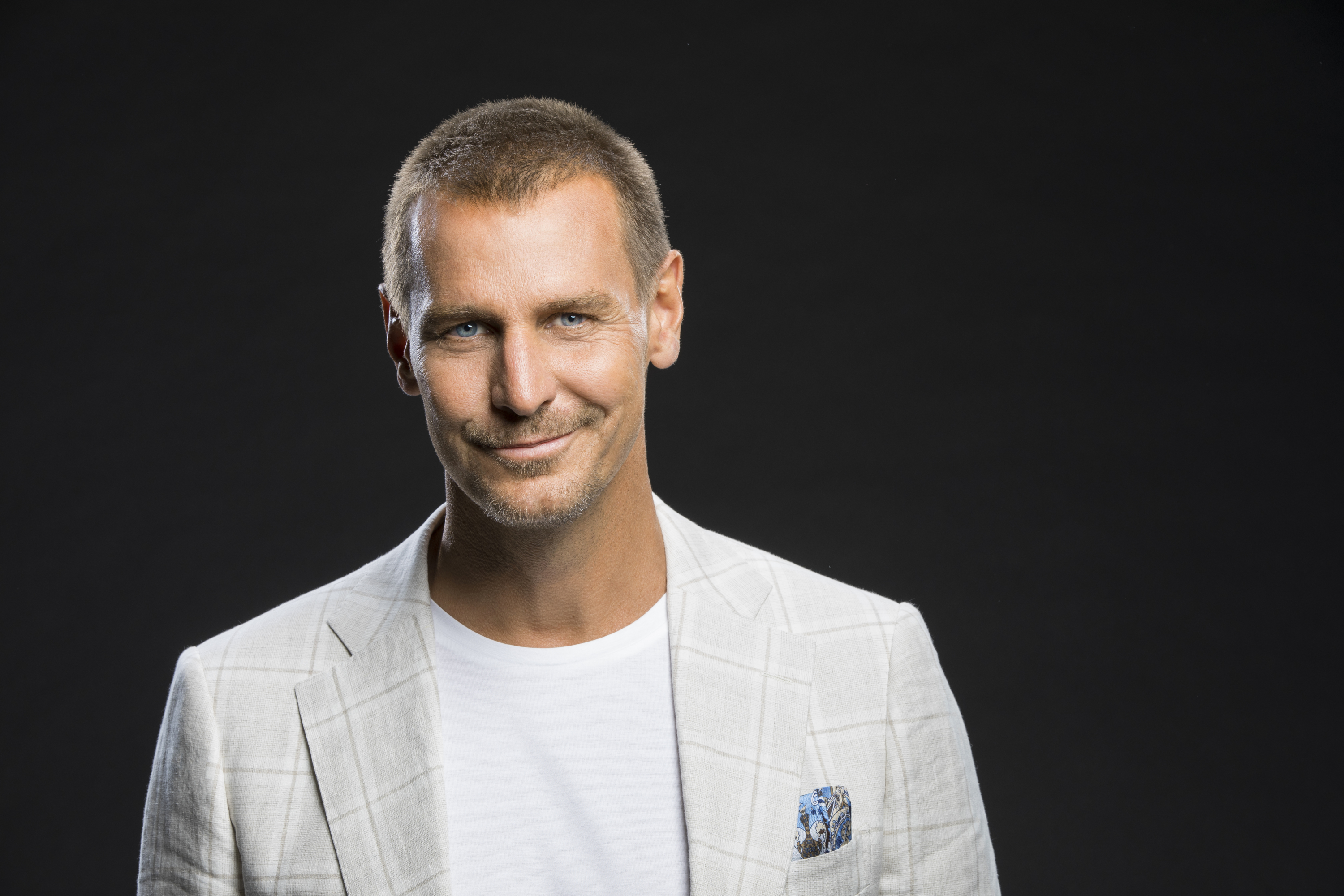 'The Bold and the Beautiful' actor Ingo Rademacher wearing a grey jacket and white shirt, and standing in front of a black backdrop.