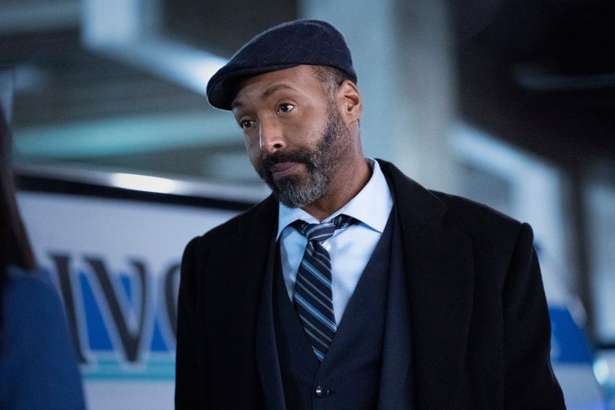 'The Flash' star Jesse L. Martin, in character as Joe West, who might be dead, wears a black coat over a dark gray suit, white button-up shirt, and blue and gray striped tie. He also wears a dark gray hat.
