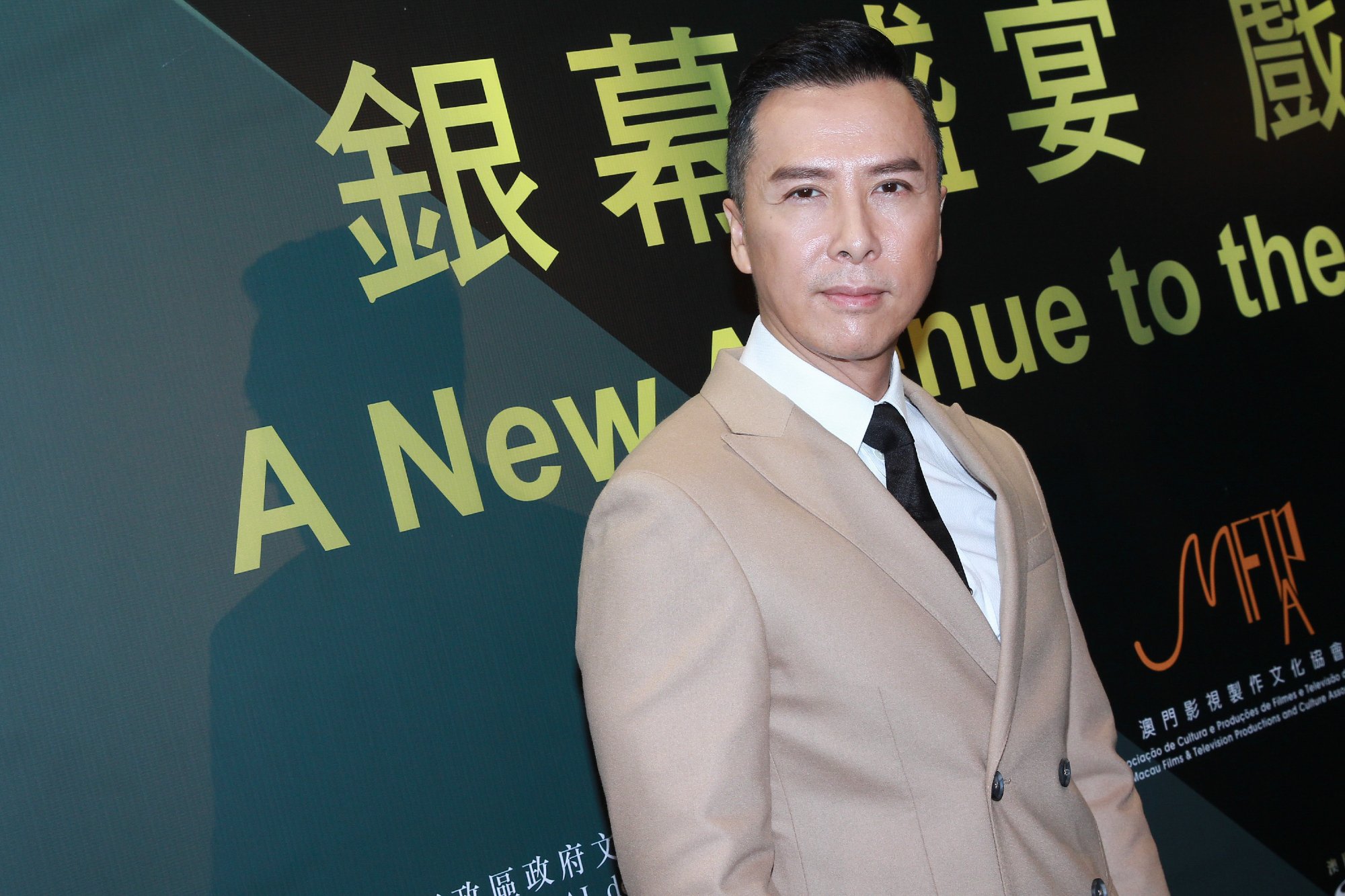 'John Wick 4' actor Donnie Yen wearing a tan suit in front of a step and repeat
