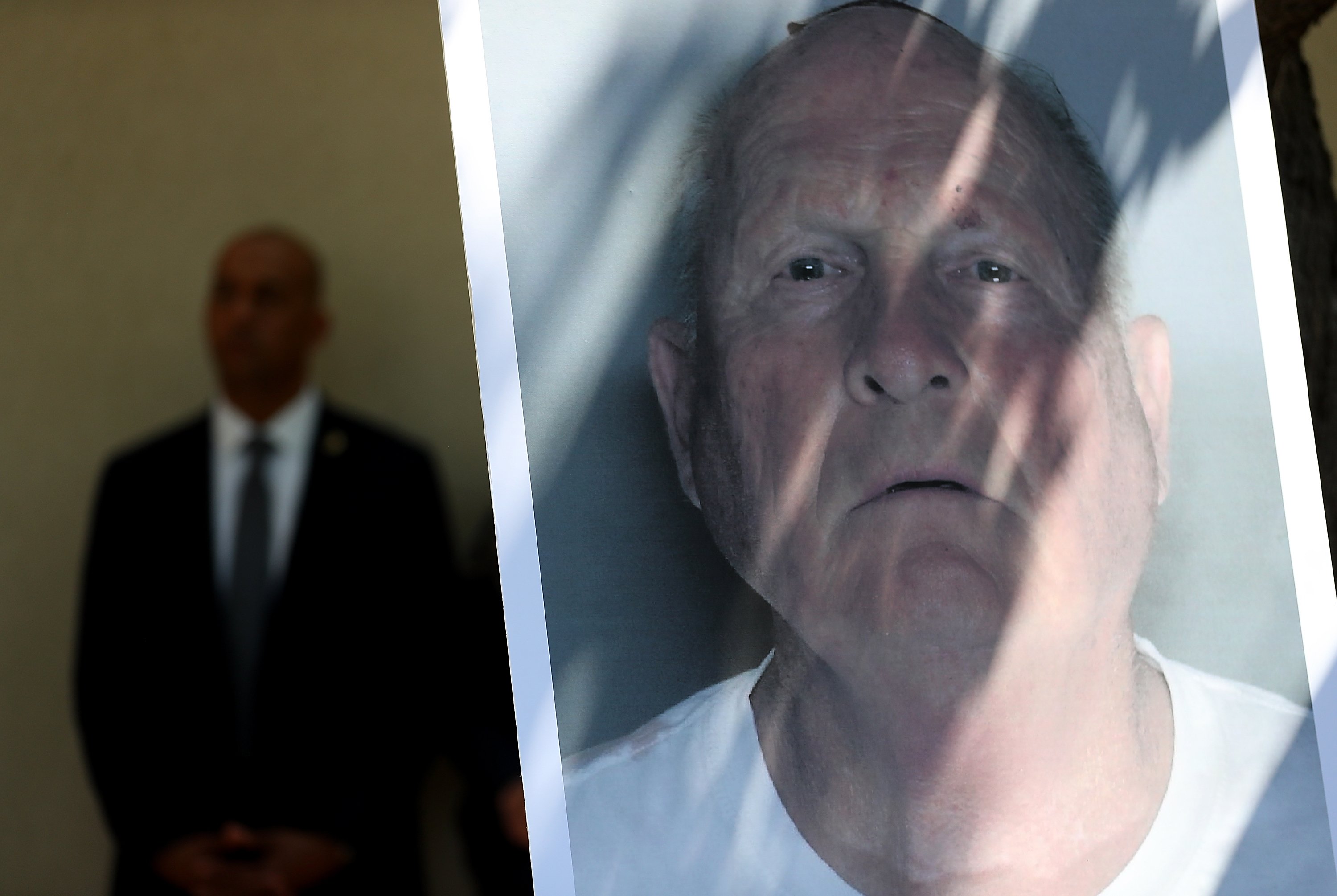 A man standing next to a mug shot of Joseph James DeAngelo