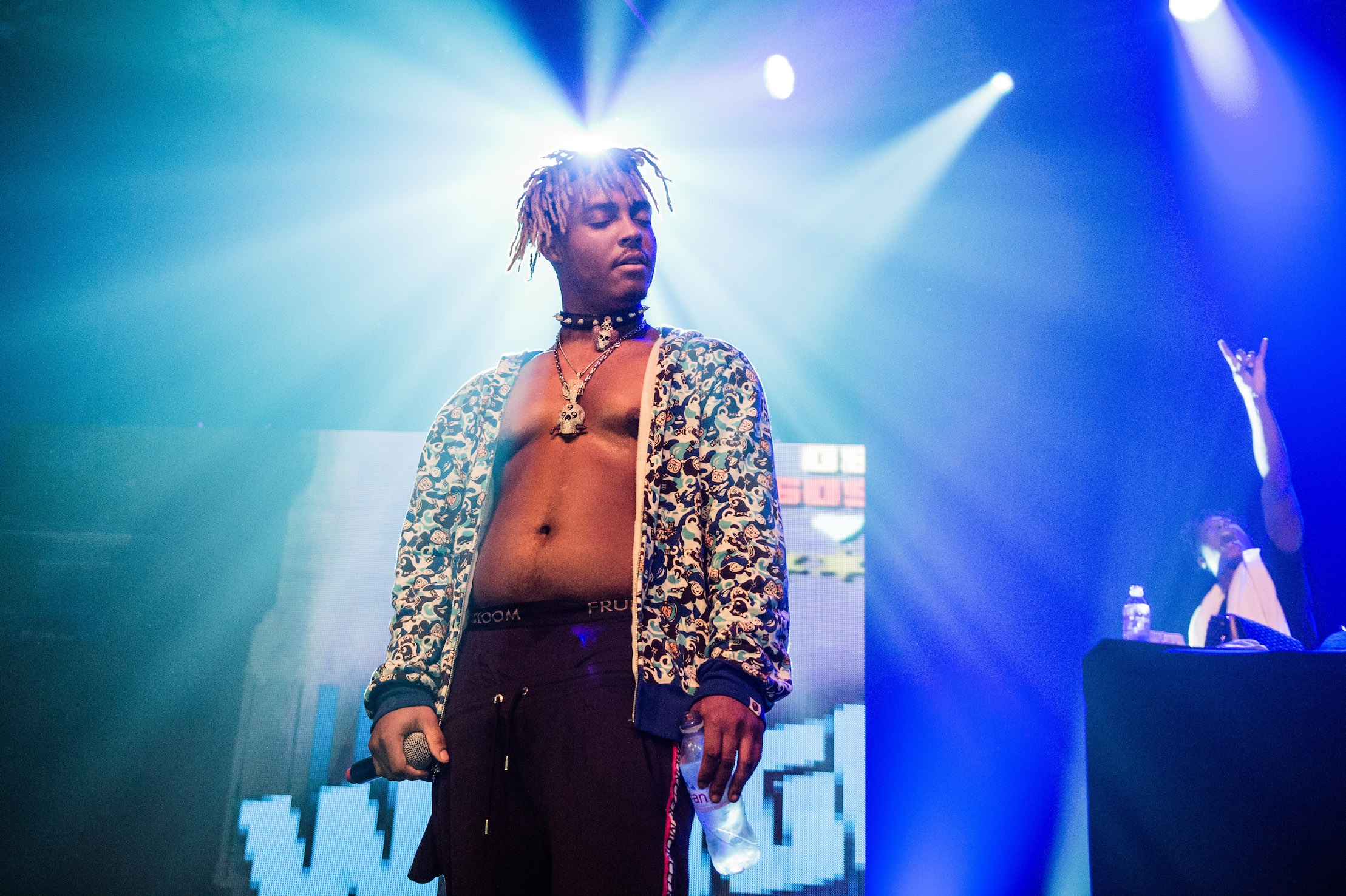 Juice WRLD performing on stage with his shirt open and eyes closed