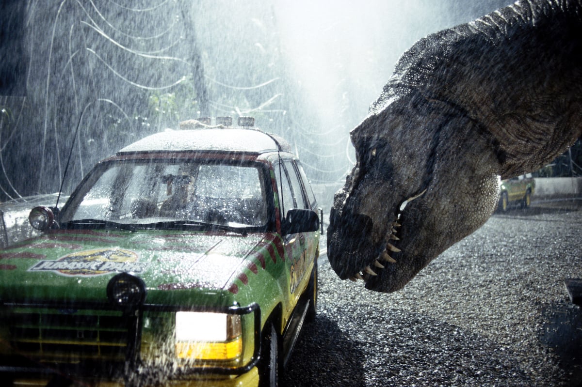 A tyrannosaurus rex terrorizes people trapped in a car during a rainy scene filming 'Jurassic Park'