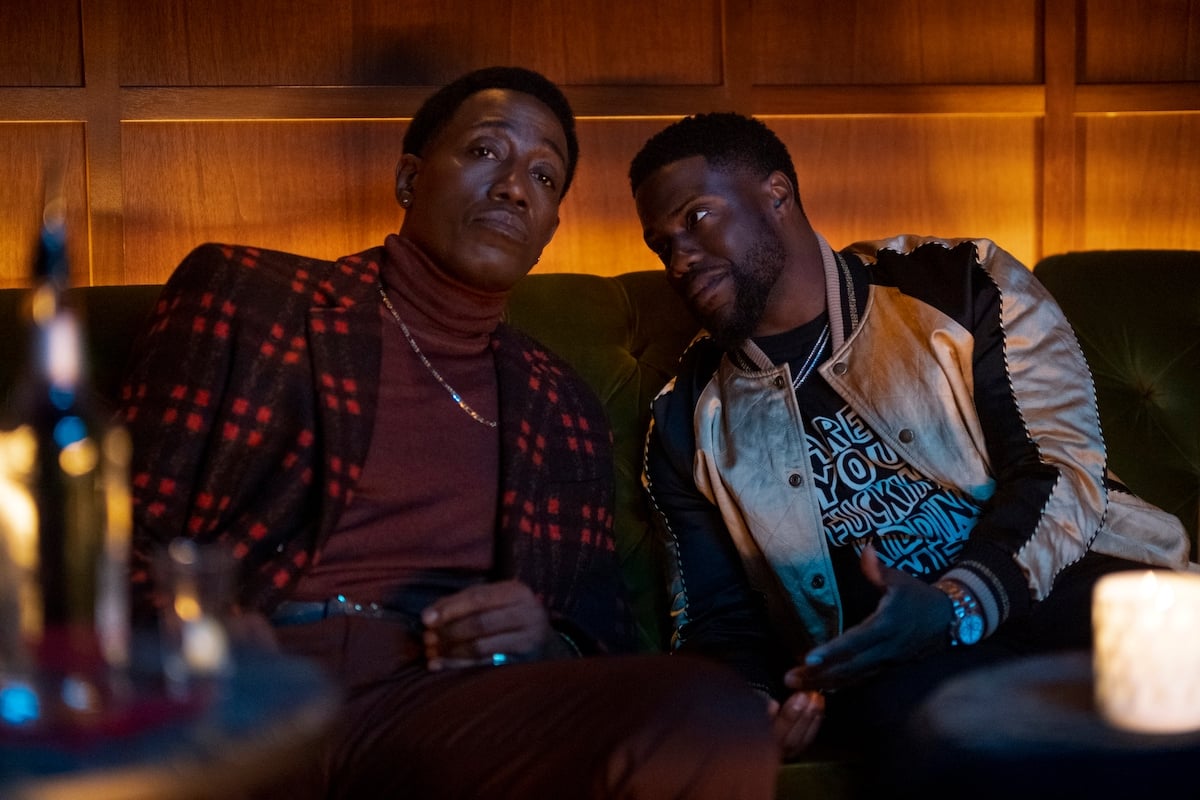 Wesley Snipes as Carlton wearing a red and black jacket with a drink in hand and Kevin Hart as Kid leaning into his brother wearing a jacket in 'True Story