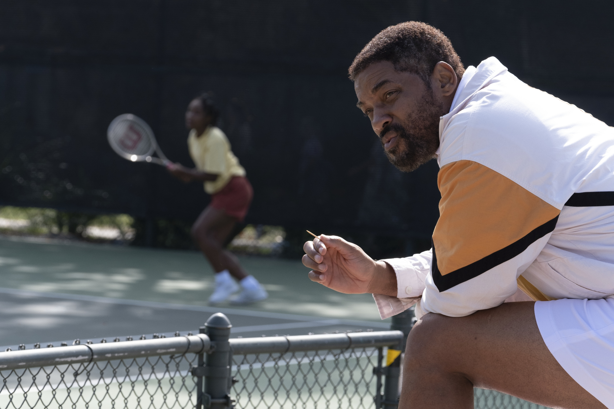 'King Richard' review starring Saniyya Sidney as Venus Williams and Will Smith as Richard Williams with Richard sitting in the foreground with Venus playing tennis in the background