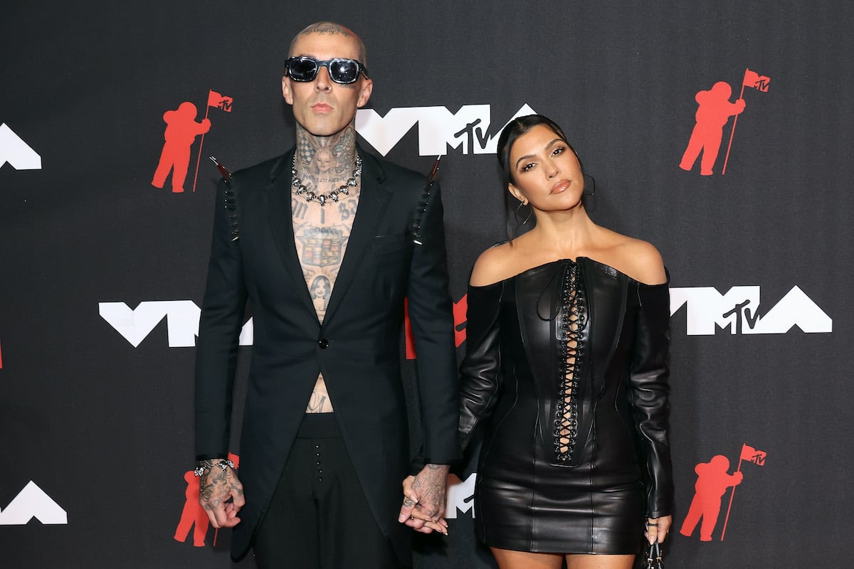 (L-R) Travis Barker and Kourtney Kardashian in front of a black wall