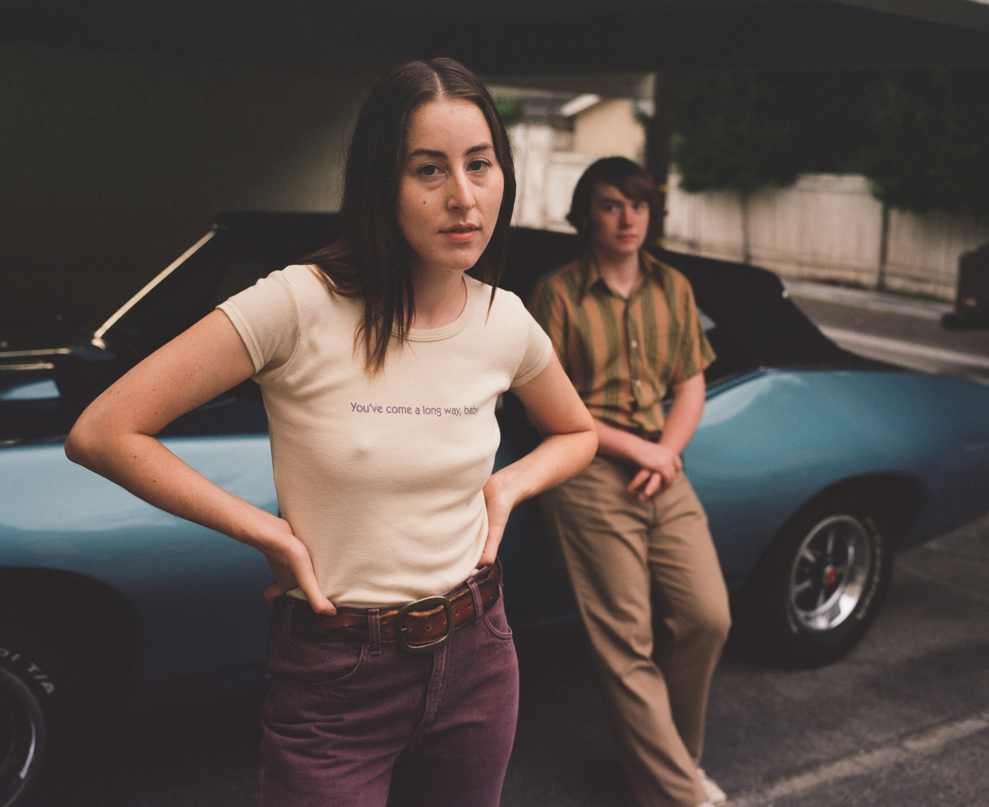'Licorice Pizza' review actors Alana Haim as Alana Kane and Cooper Hoffman as Gary Valentine standing in front of a blue car