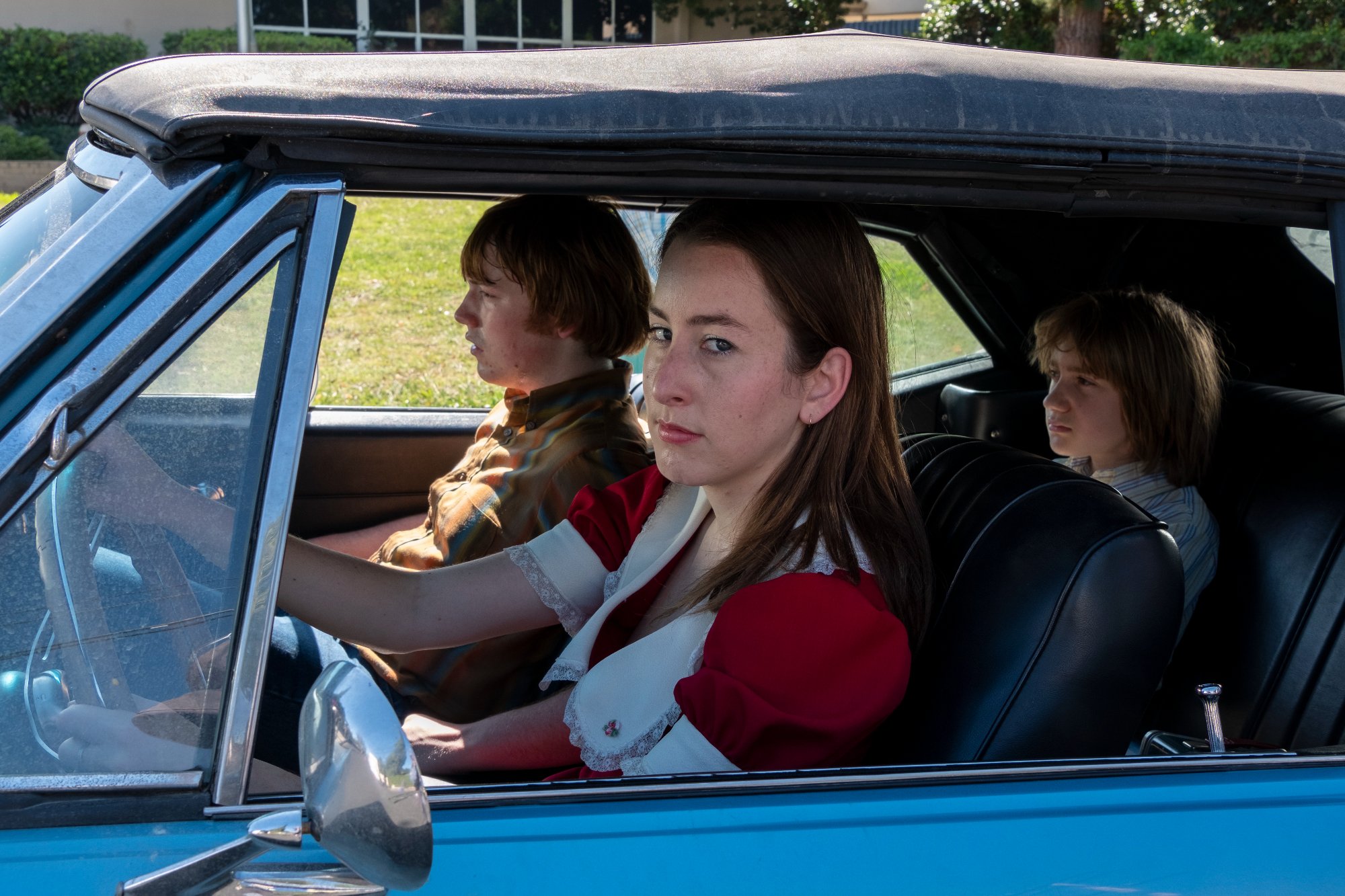 'Licorice Pizza' review actors Cooper Hoffman as Gary Valentine and Alana Haim as Alana Kane sitting in the car with grass in the background outside of the car