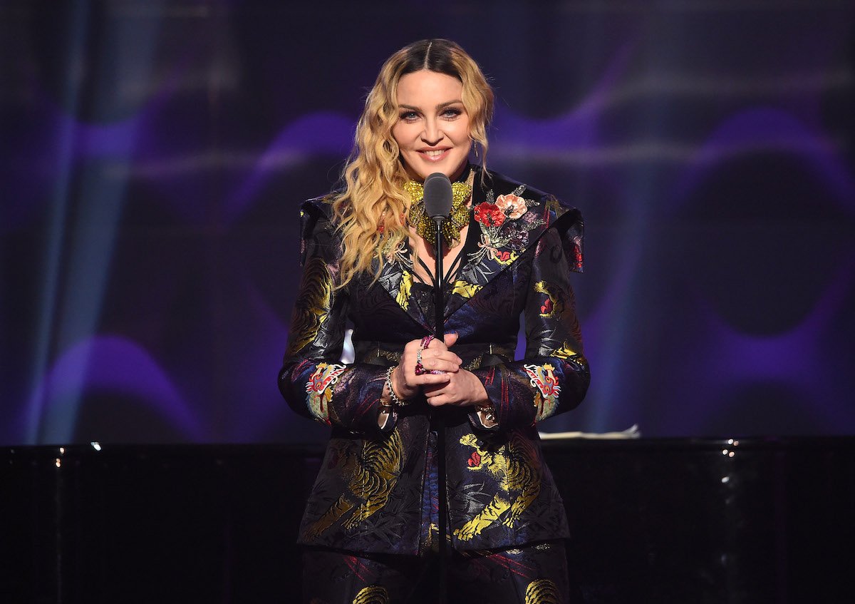 Madonna stands on stage in front of a microphone.
