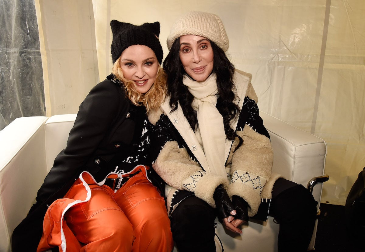 Madonna and Cher smile and pose together on a couch.