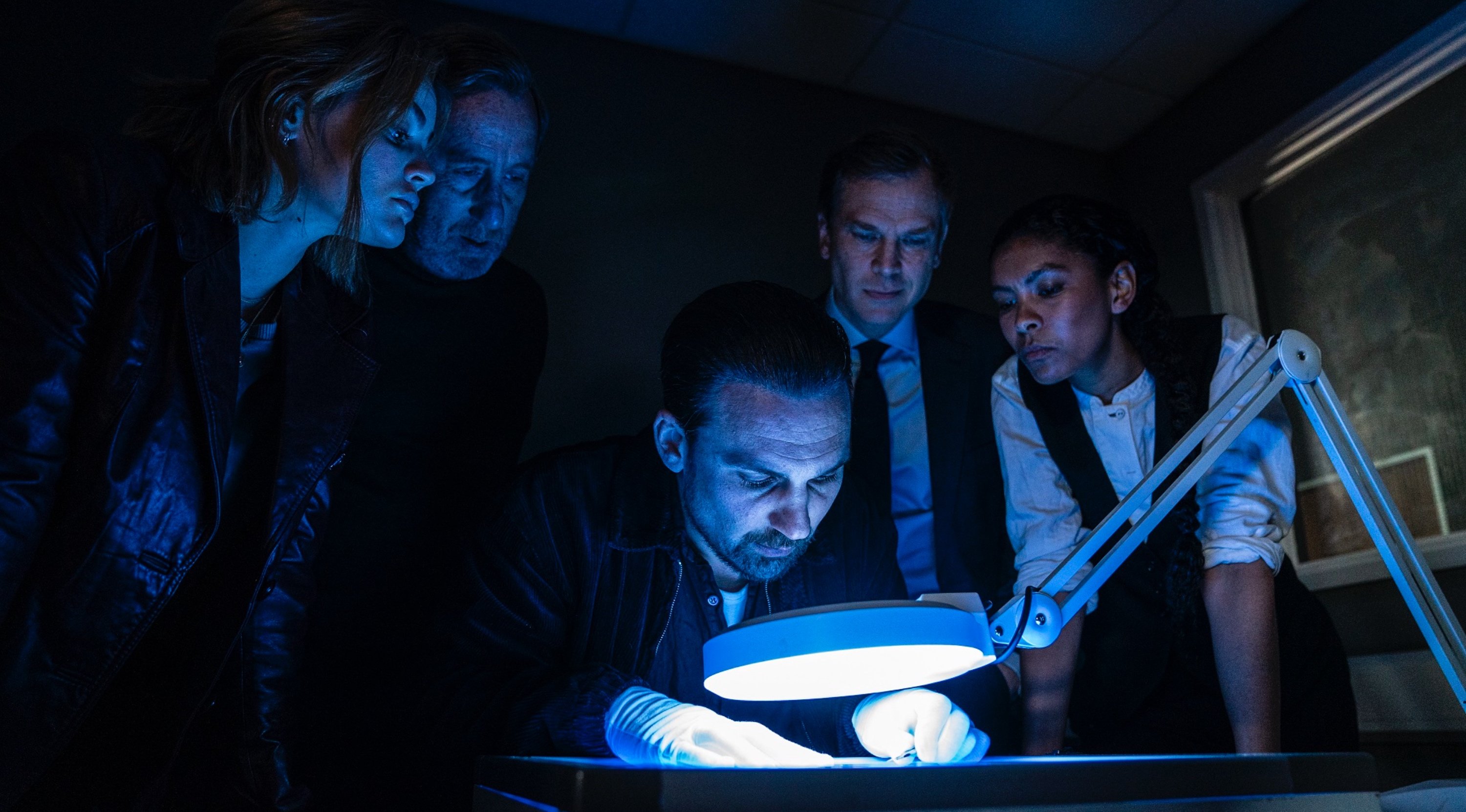 Main characters of AMC's 'Ragdoll' Episode 1 looking at envelope huddled over table.