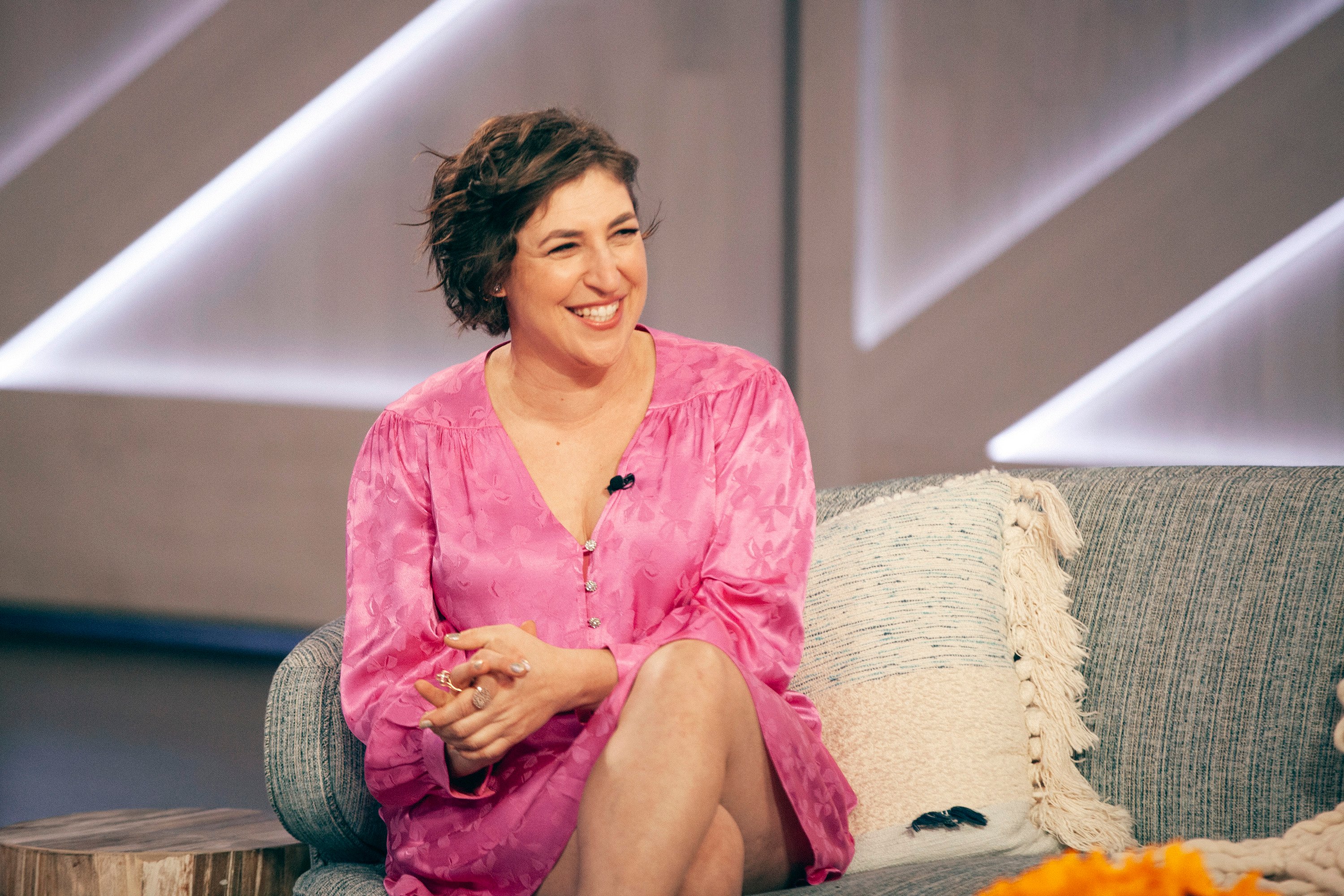 Mayim Bialik smiles on set in a pink dress