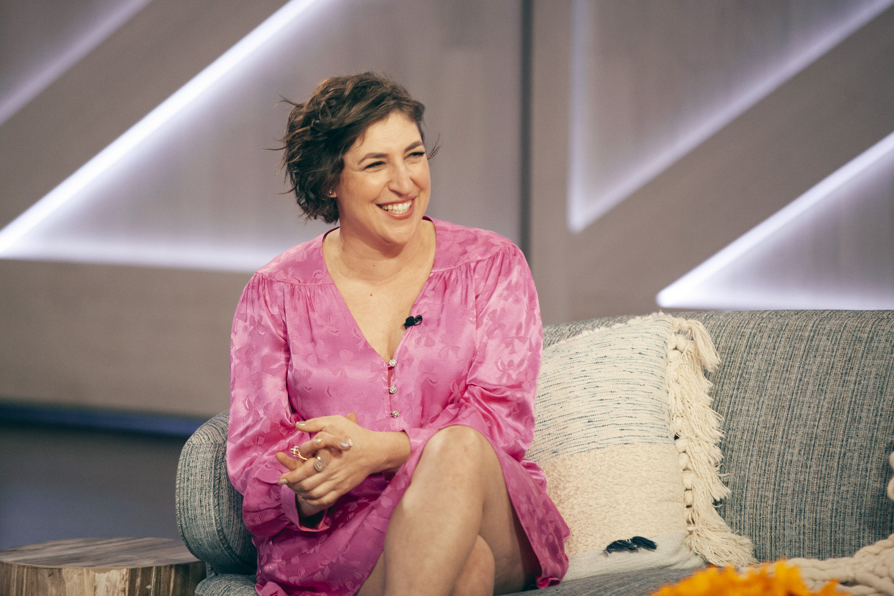 Mayim Bialik smiles on set in a pink dress