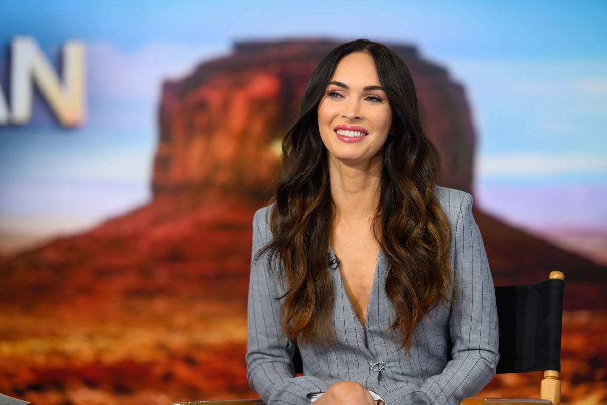 Megan Fox smiling in a silver outfit.