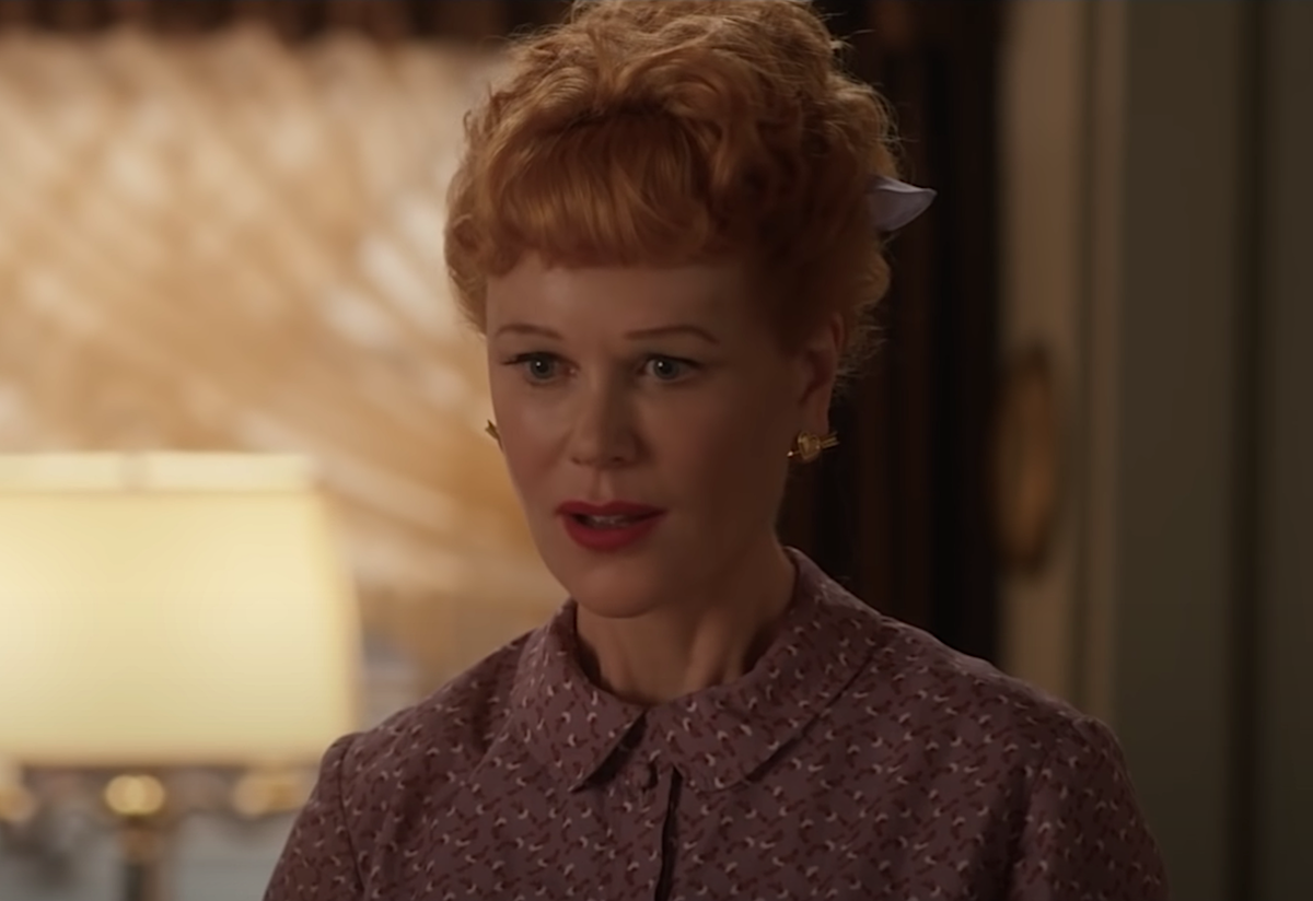 Nicole Kidman as Lucille Ball in 'Being the Ricardos.' She wears a red wig with the hair pulled back in a ponytail and a floral button-up shirt while on the fictional set of 'I Love Lucy.'
