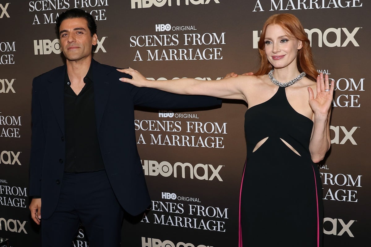 Oscar isaac and Jessica Chastainposing in a business suit and dress.