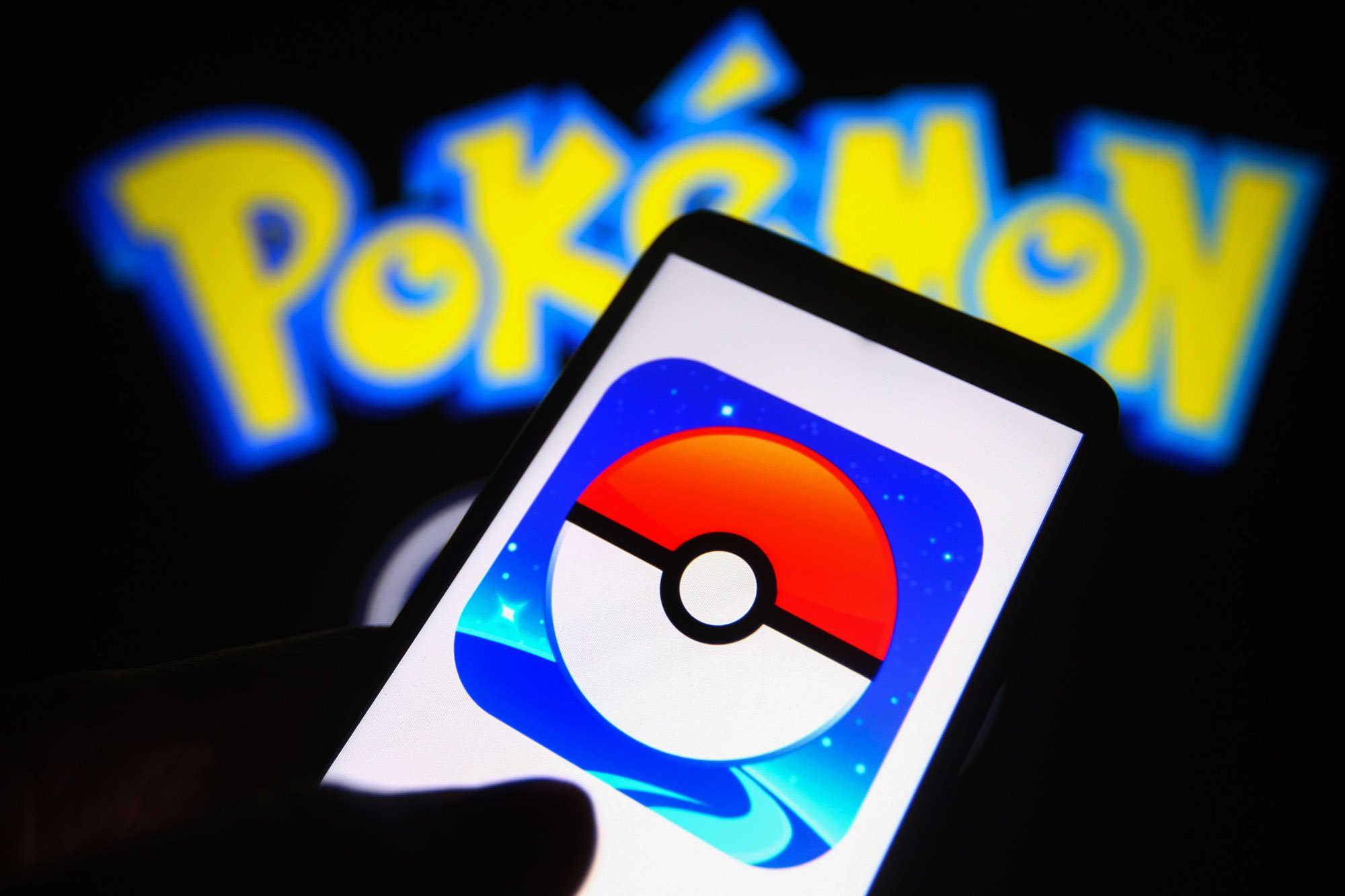 An illustration of a phone with the 'Pokémon GO' app logo on it. In the background, the 'Pokémon' logo is lit up. What will 'Pokémon GO' offer during its Festival of Lights event?