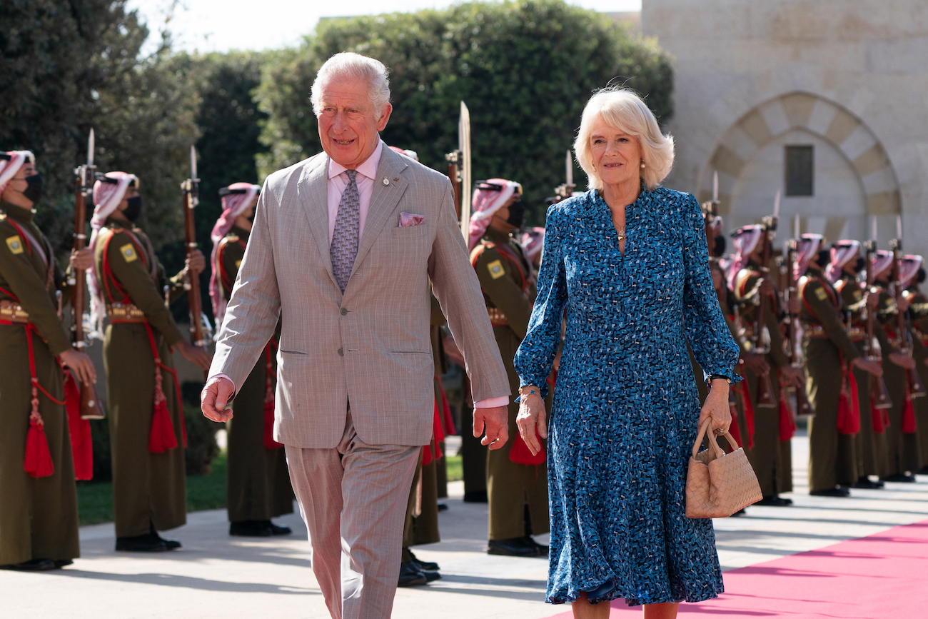 Prince Charles and Camilla Parker Bowles walk on a red carpet as they arrive in Jordan