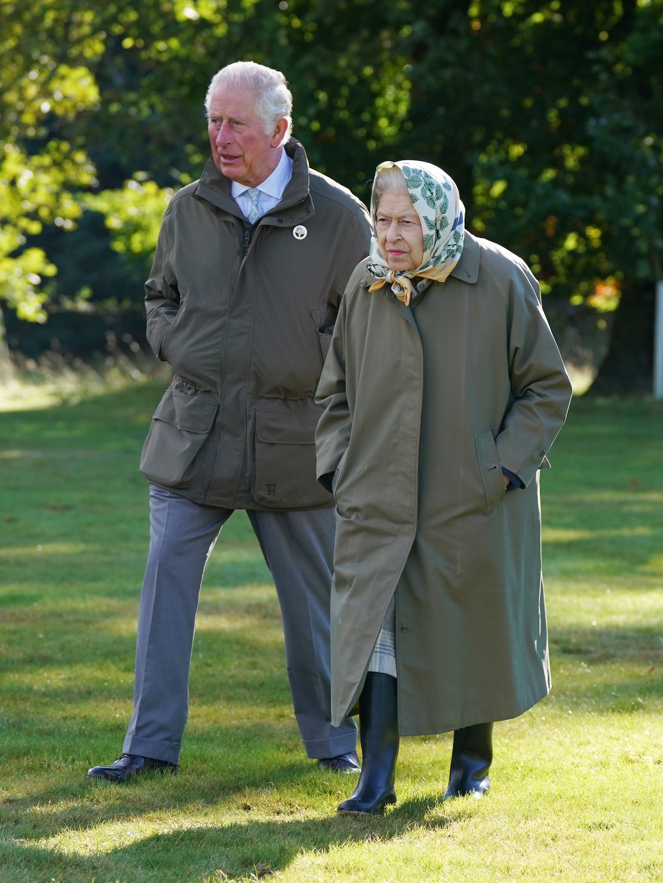 Prince Charles walks behind Queen Elizabeth II on a grassy lawn