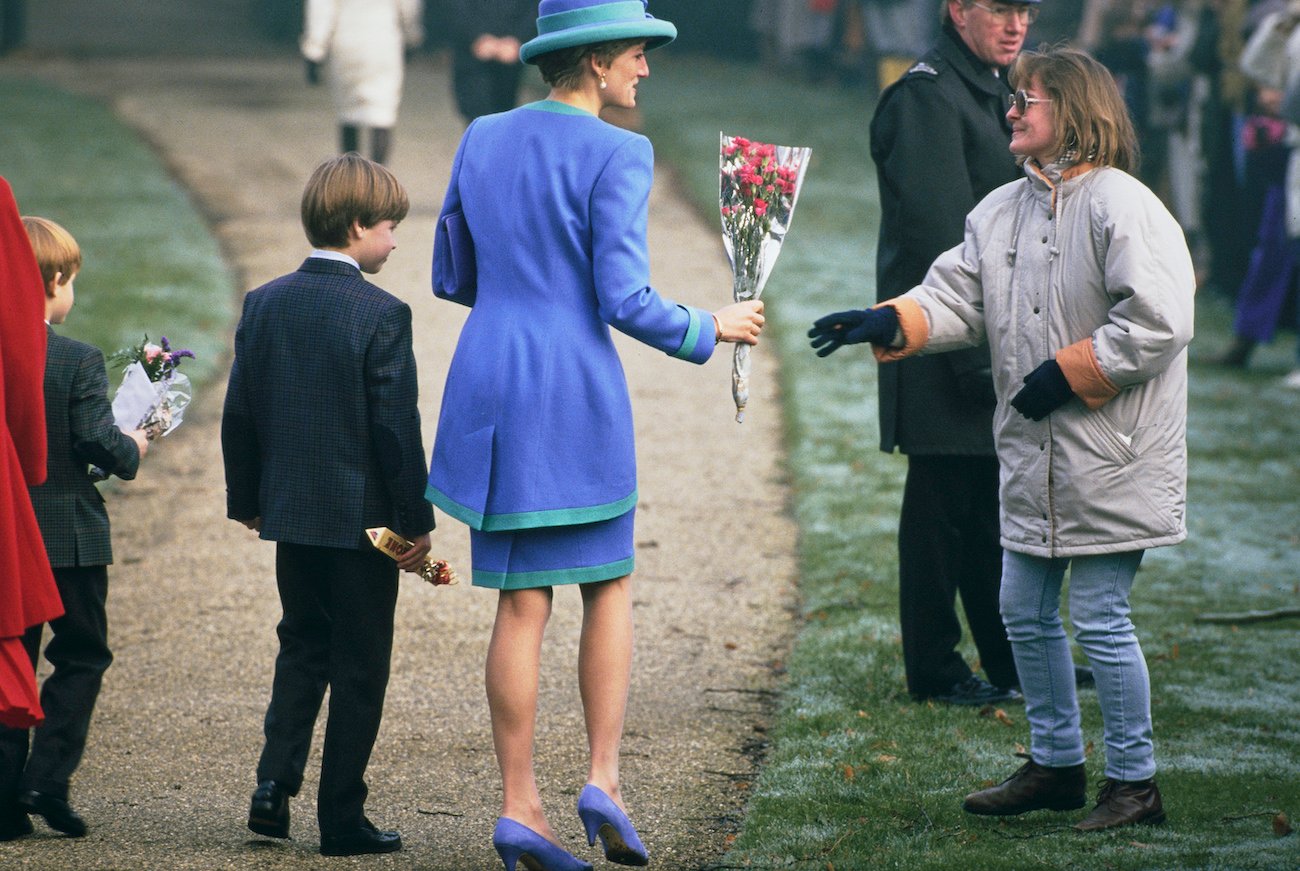 Prince Harry and Prince William stand next to Princess Diana as she takes flowers from a royal fan