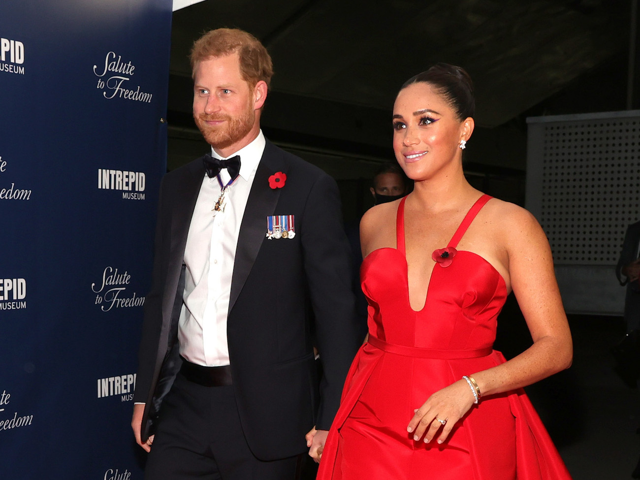 Prince Harry and Meghan Markle hold hands as they arrive at the Salute to Freedom Gala wearing a tuxedo and red gown