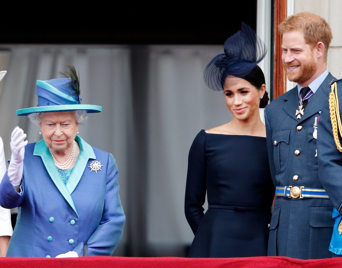 Prince Harry and Meghan Markle looking on as Queen Elizabeth waves to crowd from balcony of Buckingham Palace