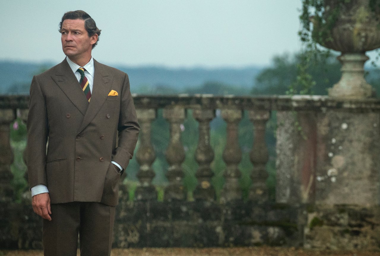 Dominic West as Prince Charles on 'The Crown' stands on a balcony in a suit.