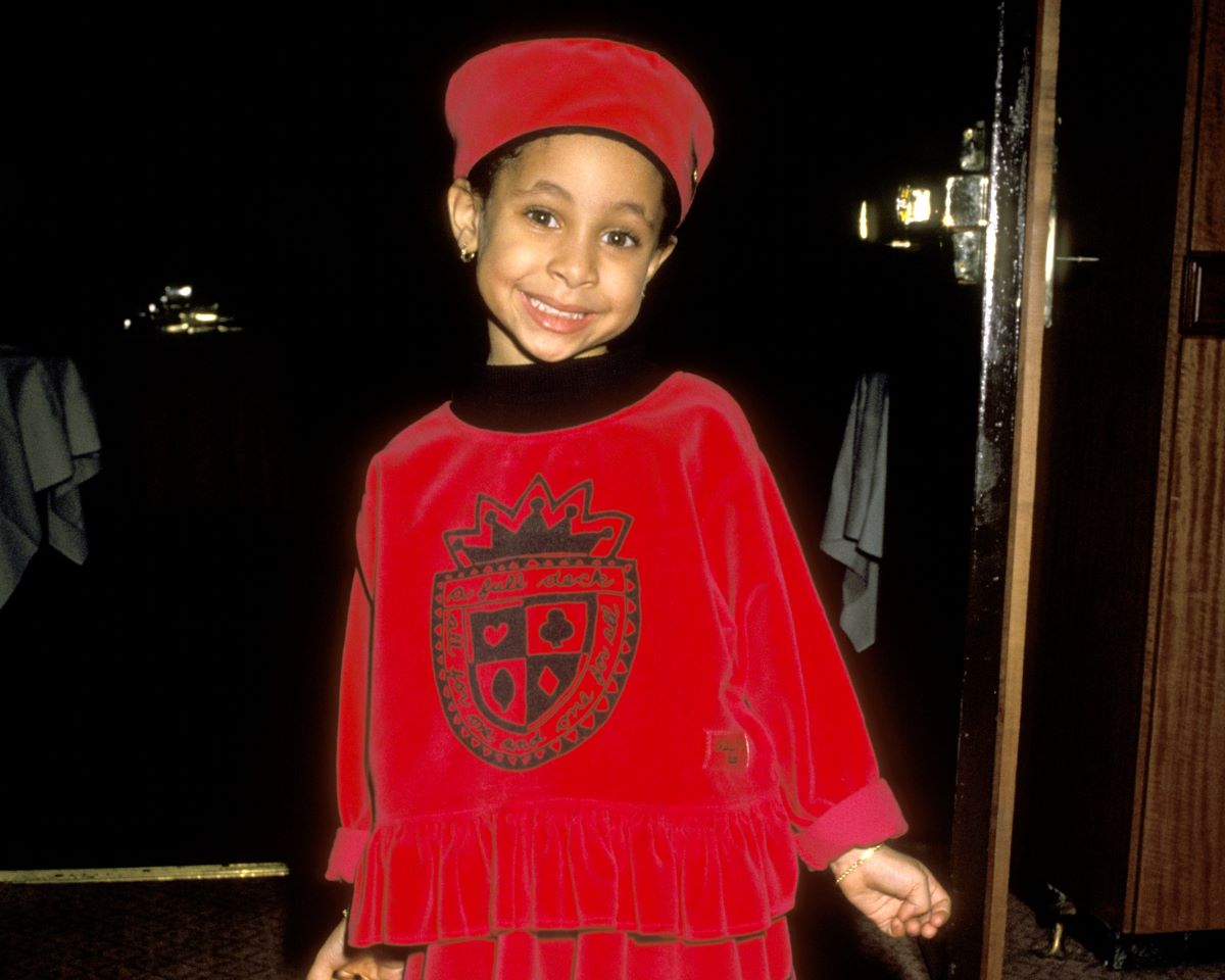 Raven-Symone c. 1990 smiling in a red outfit and matching hat