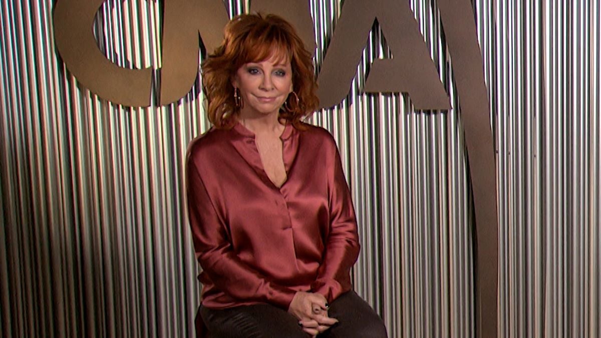 Reba McEntire seated with her hands clasped together in her lap, wearing a silky button down shirt