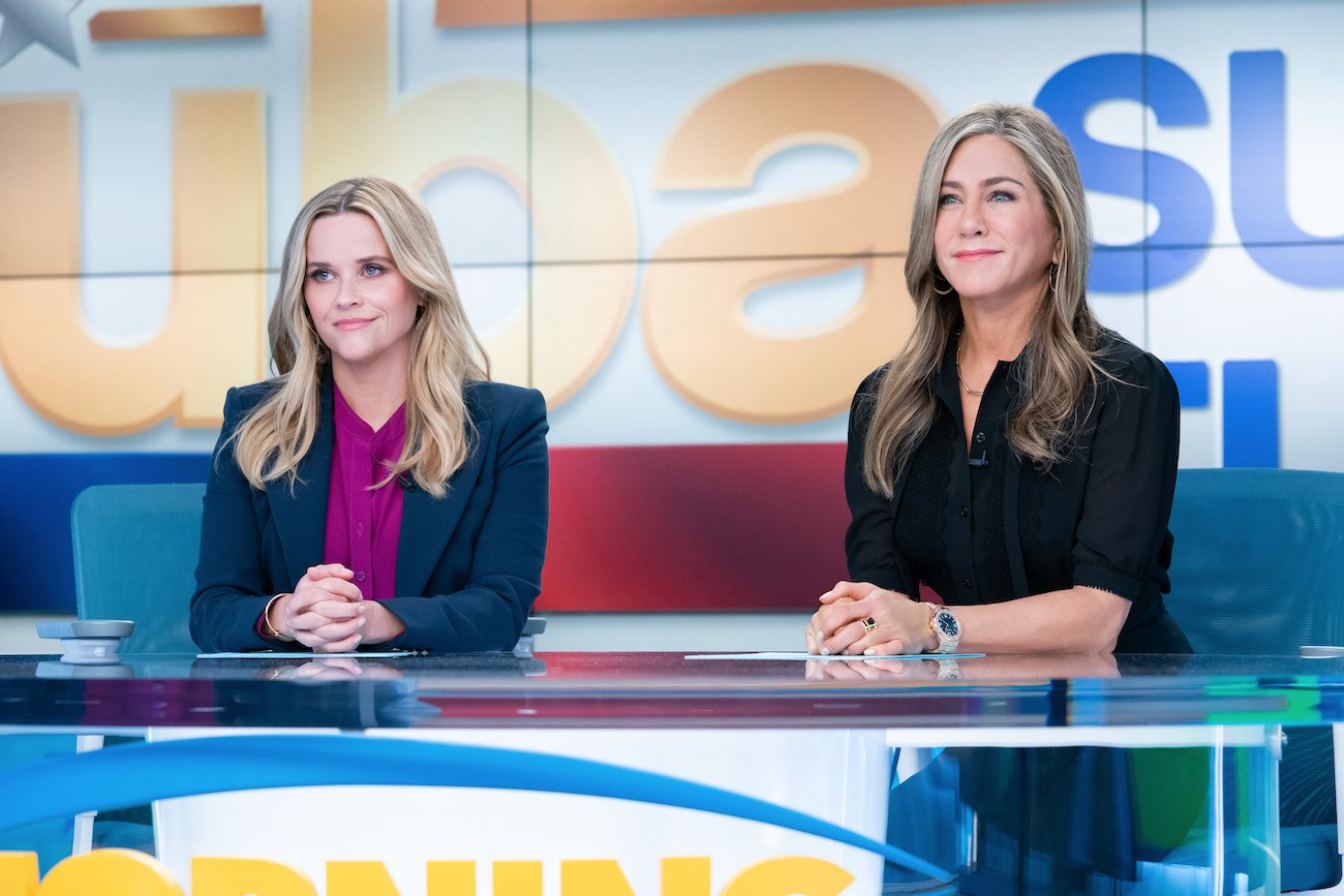 Reese Witherspoon and Jennifer Aniston sit at an anchor desk in a scene from 'The Morning Show'
