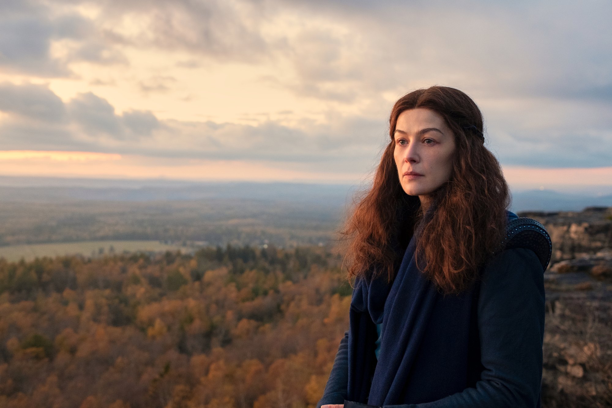 Rosamund Pike as Moiraine Damodred in Amazon Prime Video's 'The Wheel of Time' TV series. She's wearing a blue cloak and standing before a vast landscape.