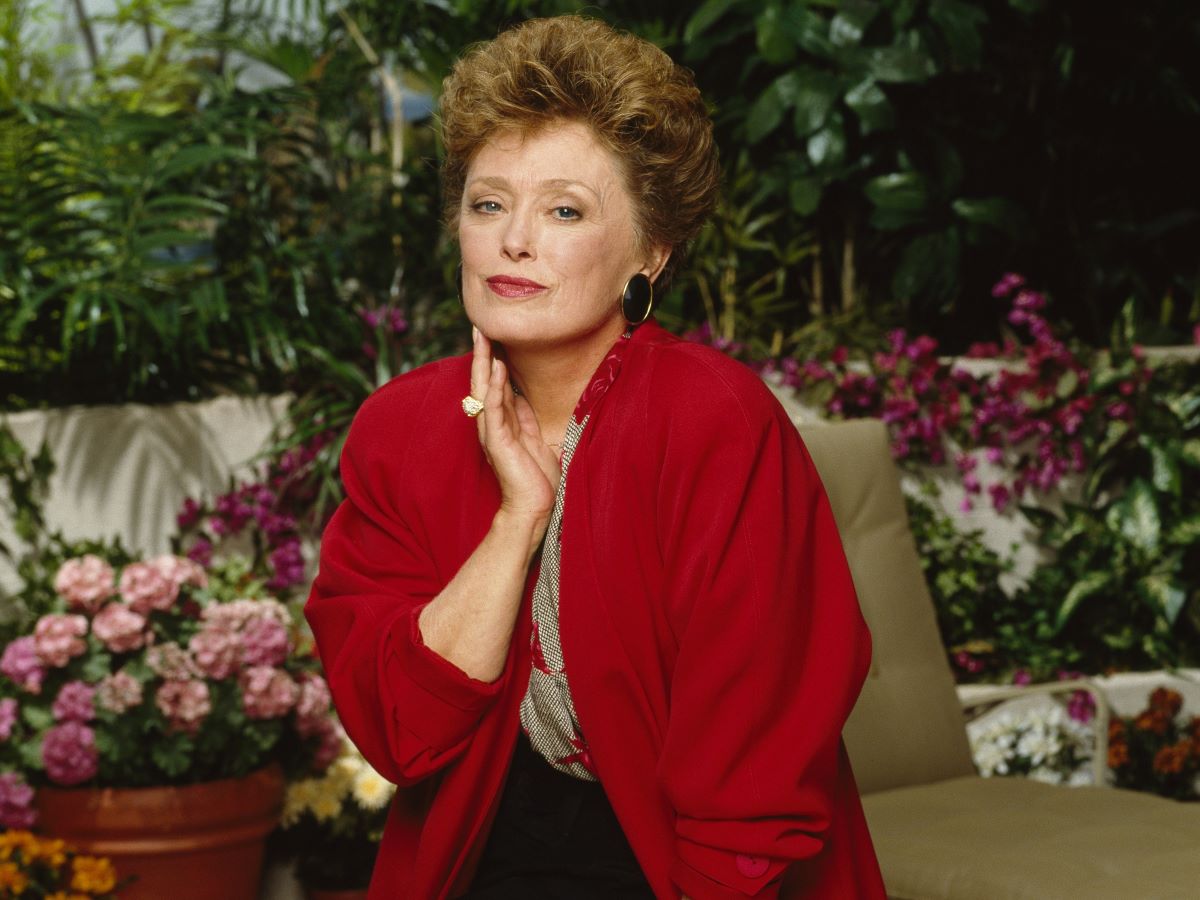 Rue McClanahan in a red blazer, touching her face with one hand