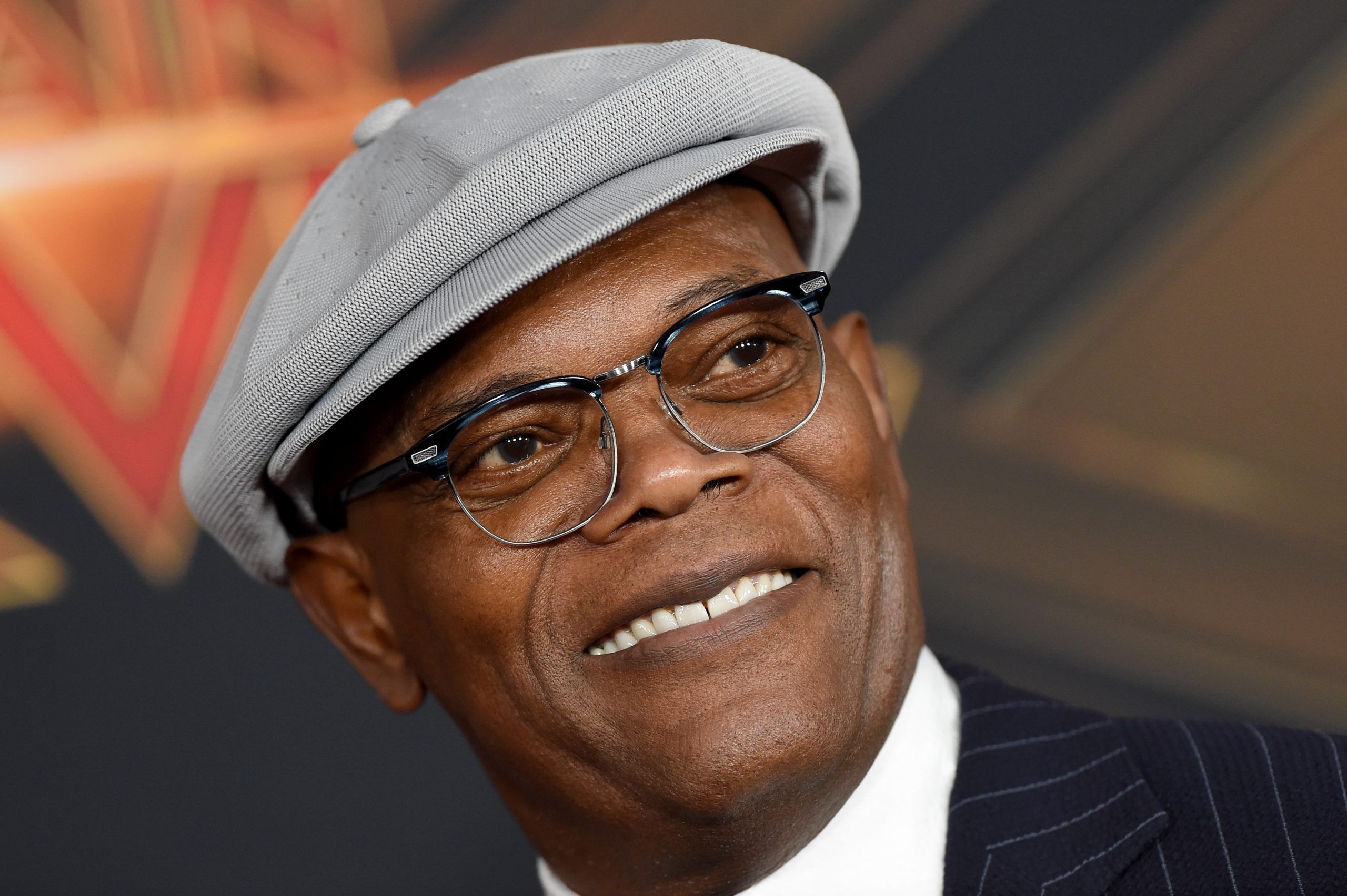 Samuel L. Jackson wearing a grey hat and suit and attending a Marvel event for his role as Nick Fury.