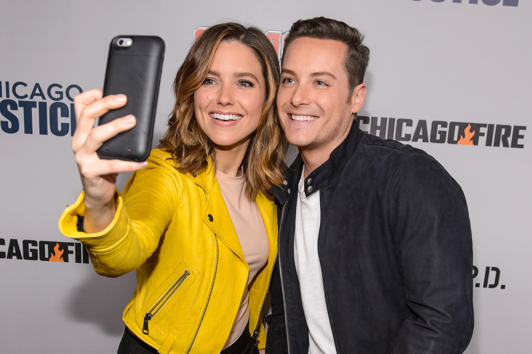 Sophia Bush and Jesse Lee Soffer smiling and taking a selfie at a 'Chicago P.D.' event
