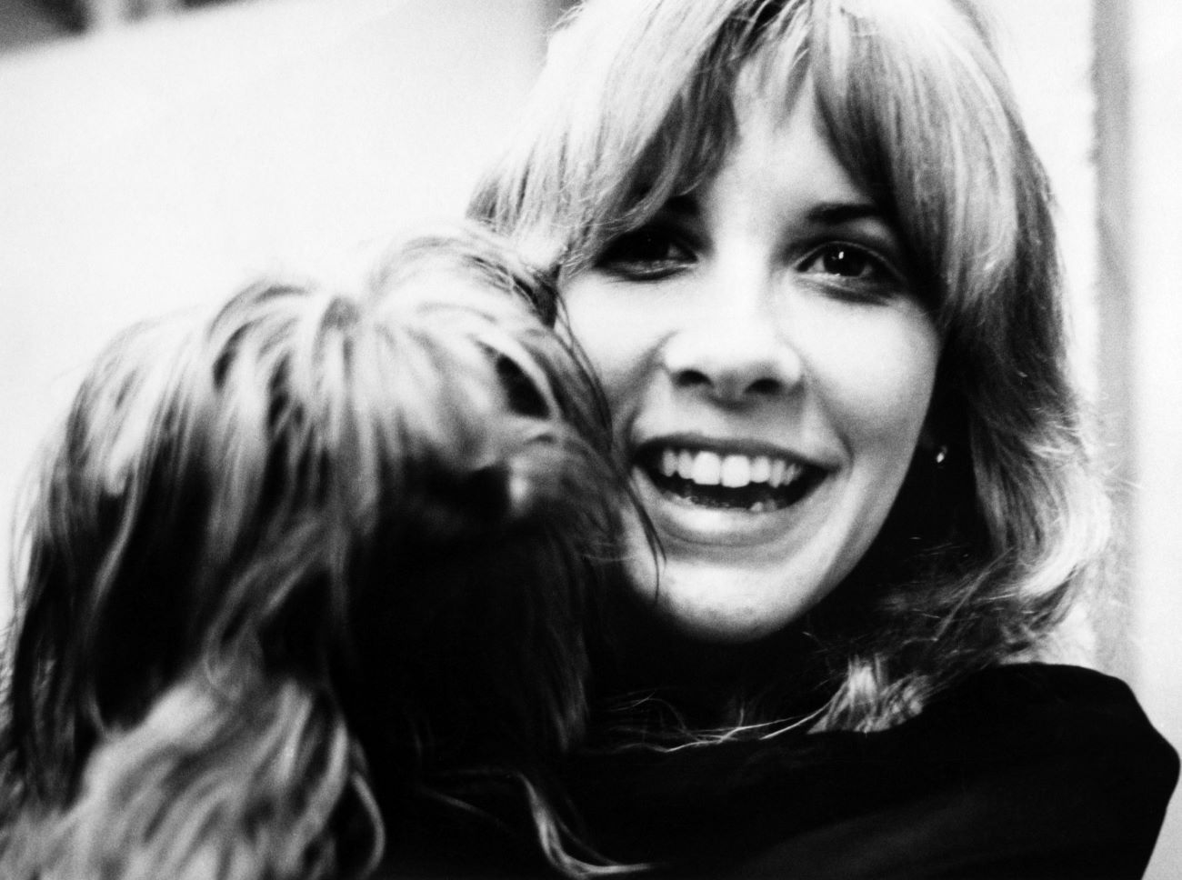 A black and white photo of Stevie Nicks smiling and holding a dog.