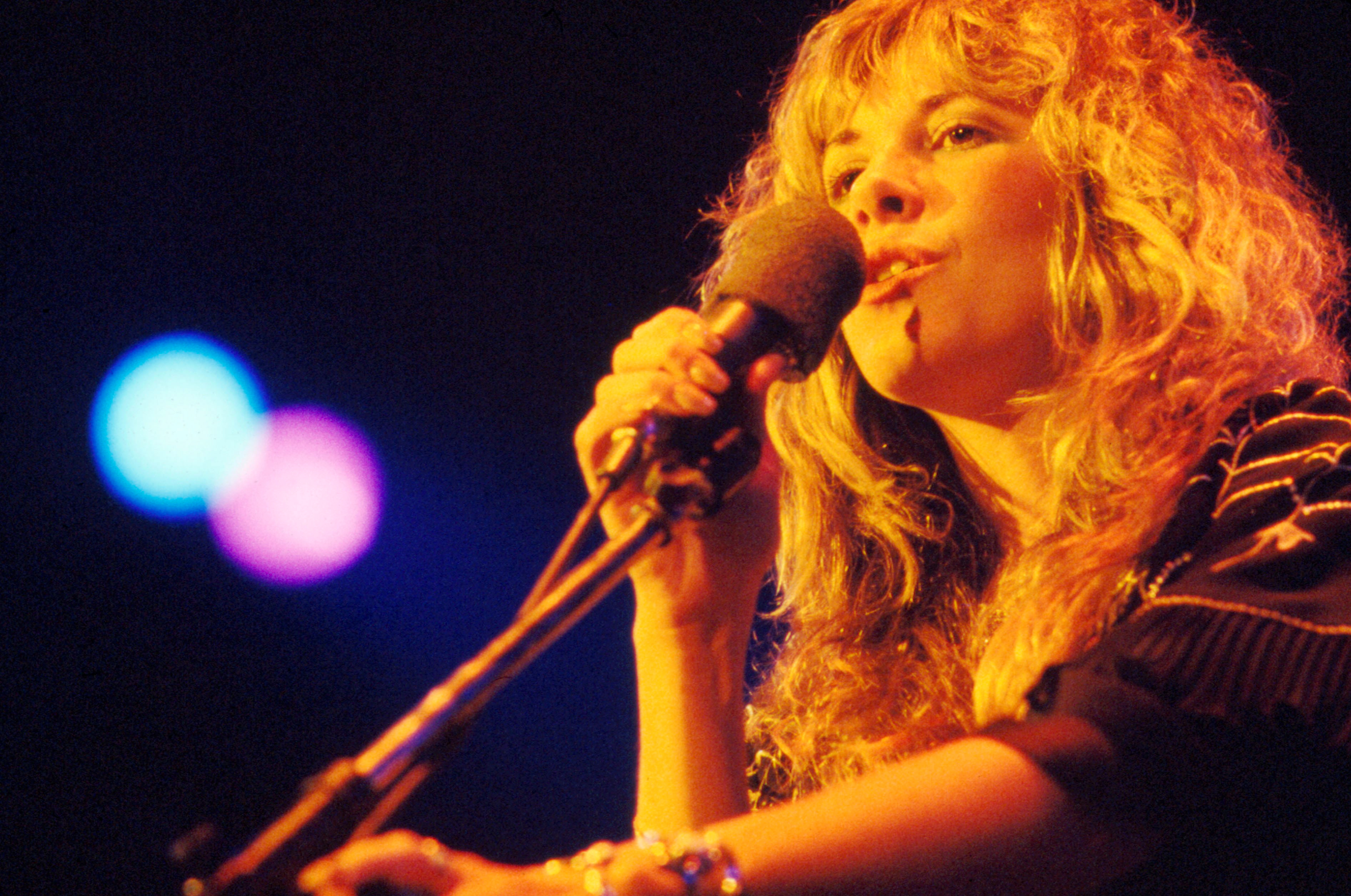 Stevie Nicks wears a striped shirt and holds a microphone.